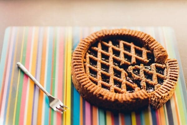 Pie with a slice cut out next to fork on a multi-coloured mat