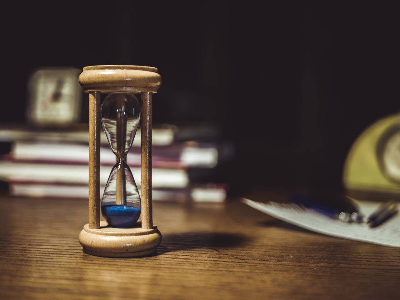 Wooden sand timer on desk with books in background