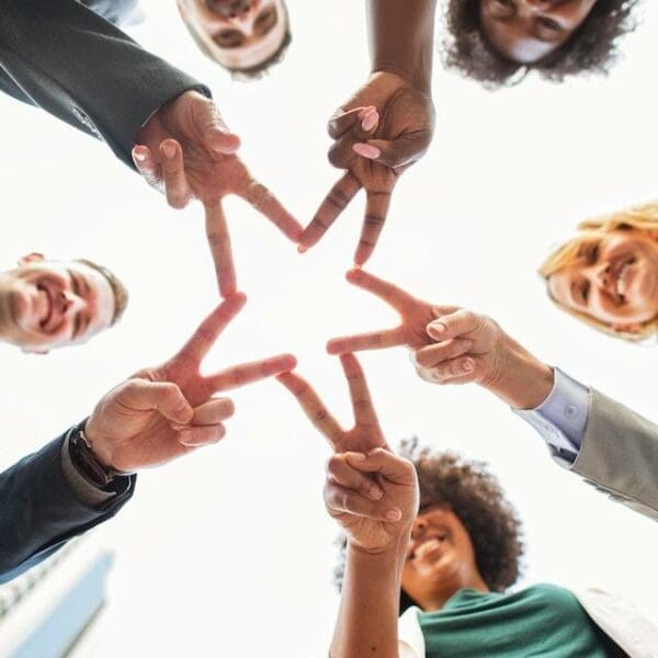 Diverse group creating a star 5 people of varying backgrounds holding their fingers out to form a star