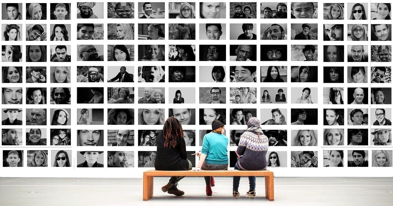 Three people looking at picture wall Three people on a bench look at a wall with pictures of diverse faces