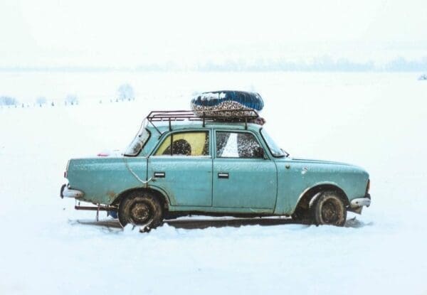 Old car stuck in snow Old blue car with luggage on roof, driving through deep snow for price wars