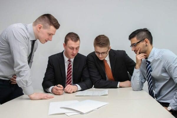 4 businessmen huddling over a document around a table 