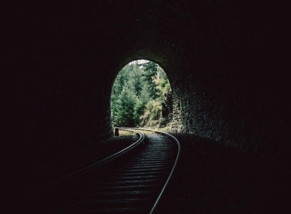 Railway inside a dark tunnel leading to an exit of light and trees represents the light at the end of a tunnel