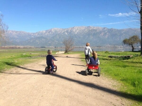 Three kids riding a bike and a cart on a picturesque field