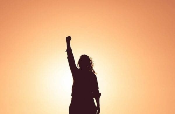 Silhouette of a woman with her first in the air with bright orange background