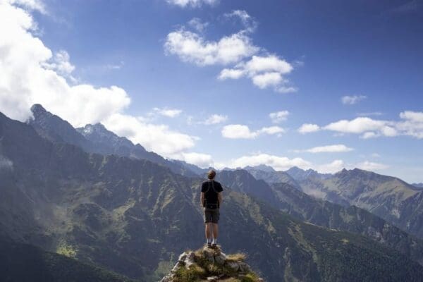 Man on the edge of a cliff looking at the view of a mountain landscape for emotional wellbeing