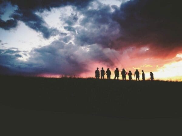 Silhouette of nine people standing in a field watching the sunset