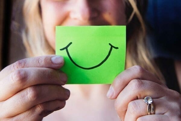 Woman holding a sticky note with a hand-drawn smile to hide her mouth
