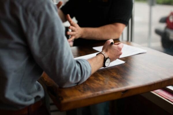 Two businessmen talking while writing down notes at a wooden table