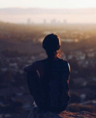 Person sitting on cliff looking out over a city