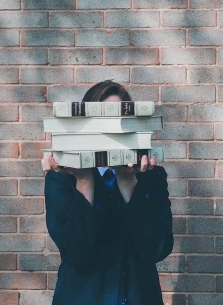 Lady in black holding 4 thick books with both hand so they cover her face 