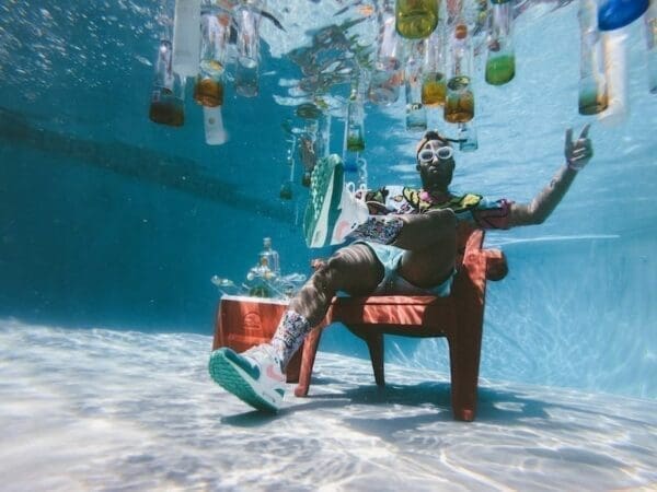 Man in party attire sitting on a chair underneath the pool with alcohol bottles