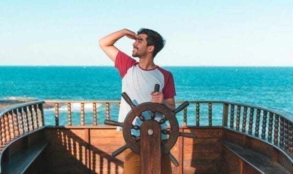 Man in a ship holding a captain's wheel in the middle of the sea