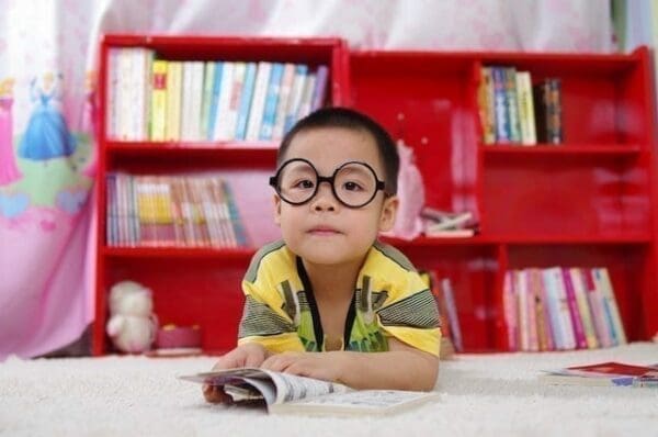 Young boy with glasses reading with red book shelf in background