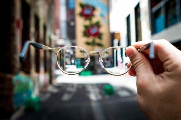 Hand holding a pair of glasses before a building scene