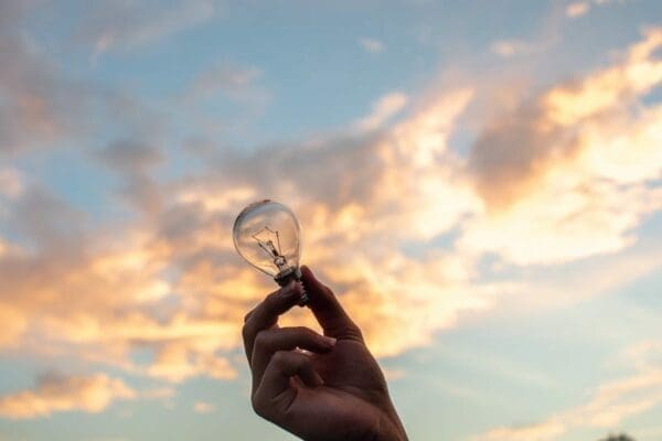 Hand holding clear lightbulb aloft against the backdrop of the sky 