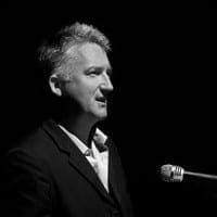 James Kerr James Kerr in a black and white setting with a microphone before him