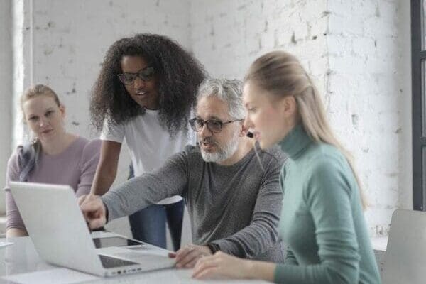 Manager coaching three female employees using a laptop displays coaching skills for managers