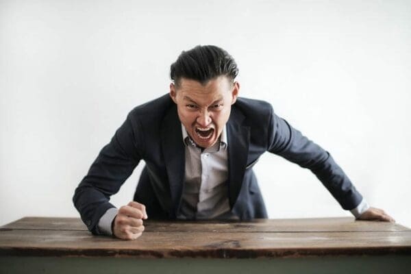 Angry businessman with fist on table yells commands 