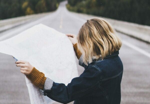 Woman in the middle of a road looking at a large map as she strategizes