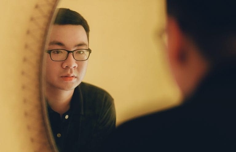 Man with glasses practices verbal communication in a mirror
