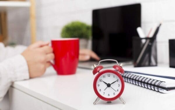 Red alarm clock on office desk next to hand holding a red cup