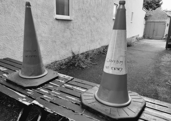Black and white picture of traffic cones labelled with Covid 19 No Entry