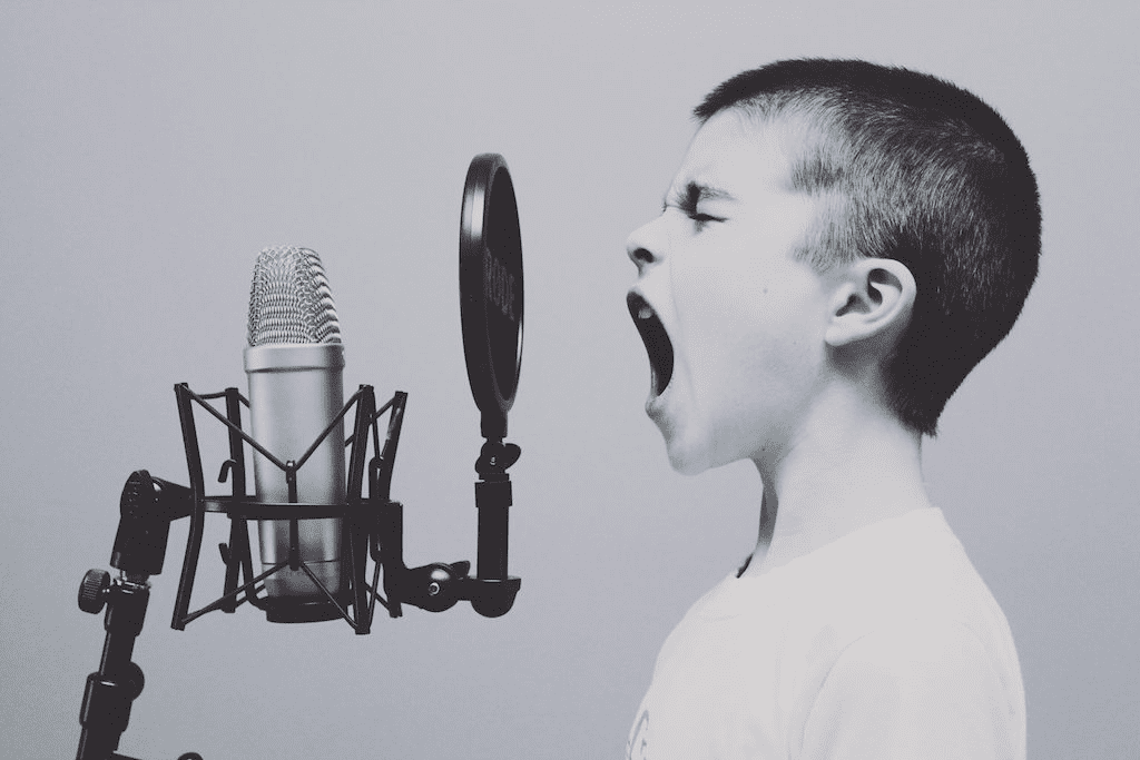 Black and white picture of young boy shouting into recording-style microphone