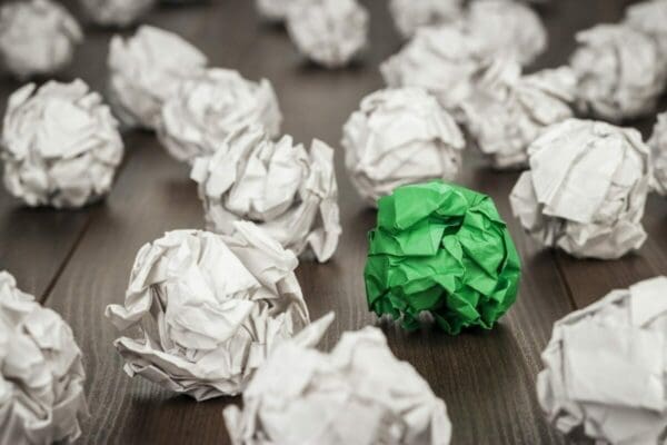 Single red crushed paper ball among white paper balls