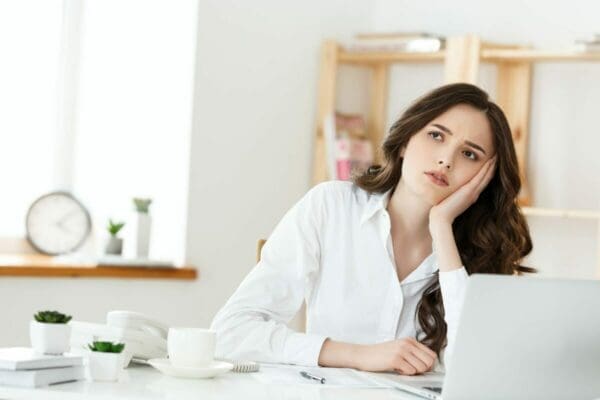 Woman at her desk with her hand at her jaw is demotivated from poor leadership