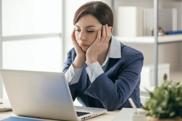 Businesswoman at desk looking bored with hands at her jaw and watching presentation on her laptop