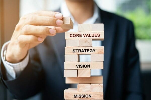 Businessman placing a wooden block on a Jenga tower that has the words core values, strategy, vision, and mission