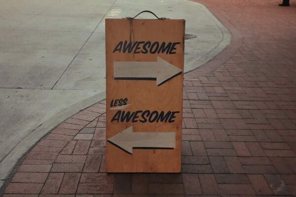 Wooden sign in the street with Awesome pointing right and Less Awesome pointing left 