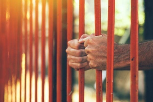 Man's hands on red bars represents barrier