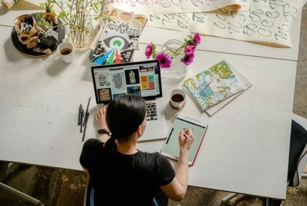 A top view of a female designer working at a table with a laptop and tablet