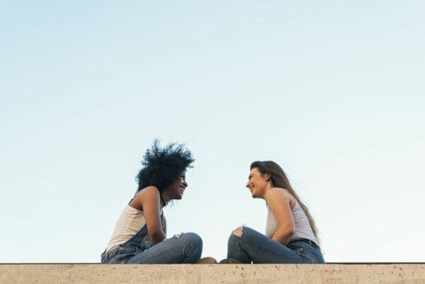 Women sat outside on the ledge of a building mirroring eachother's body language 