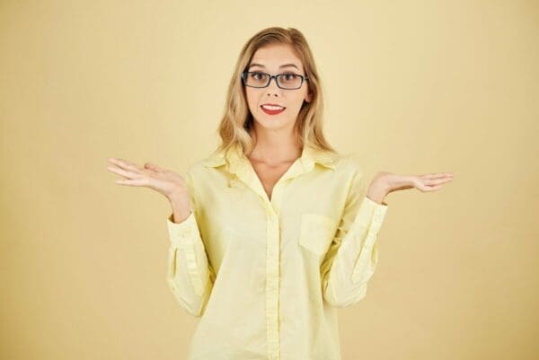 Young woman with an I don't know expression and both palms open with yellow background