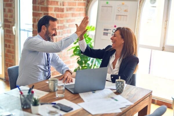 Manager and employee high-fiving over laptop and papers for Ethics in Management