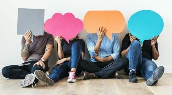 Four employees seated on the ground holding up colored speech bubble cutouts representing employee feedback