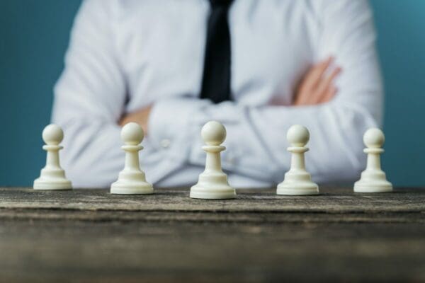 Five white chess pieces with folded arms from businessman in background thinking about Post-Covid Business strategy