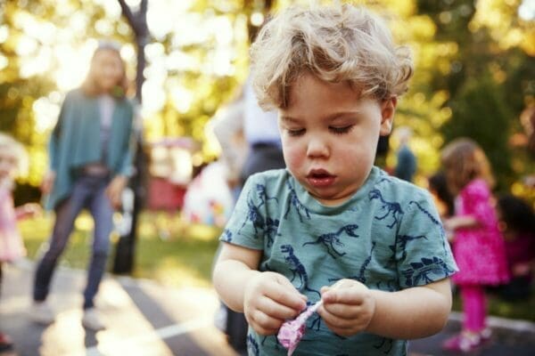 Toddler boy unwrapping a lollipop in a park outdoors for meaning we give to words