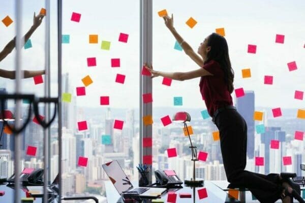 Businesswoman standing on desk attaching sticky notes to window