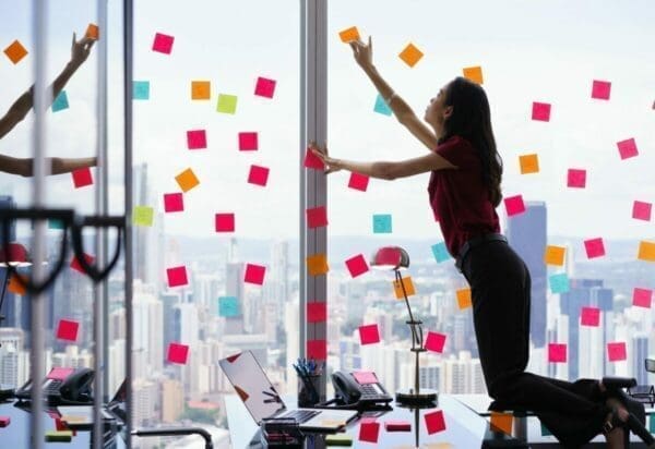 Woman standing on a desk, attaching sticky notes to window