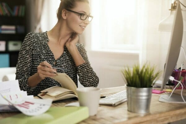 Woman writing list in a time management diary whilst looking at her computer