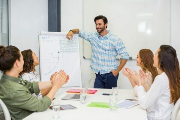 Manager standing beside presentation board while coworkers clap