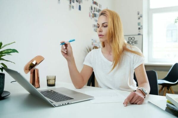 Woman working from home points to her laptop while writing emails 