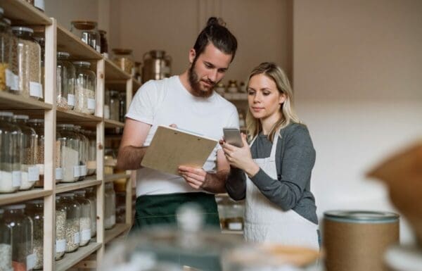 Two shop assistants wearing aprons checking store visit data on a clipboard