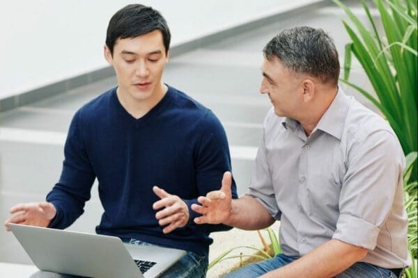 Businessman using a computer speaking to a male mentor