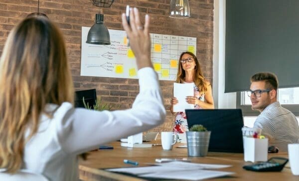 Female manager with one hand raised is answering a one option question in a work meeting