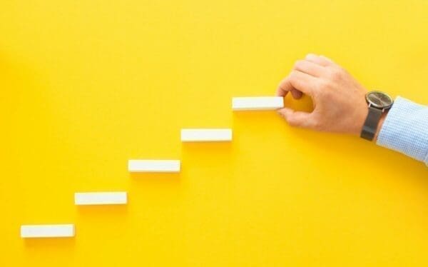 Hand making a stairs with white blocks to represent improvement